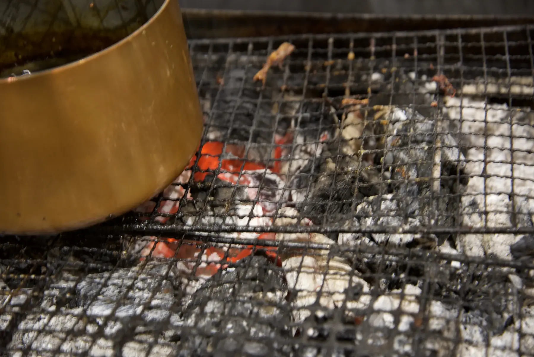 Charcoal glowing red beneath the grill, beside a copper pot